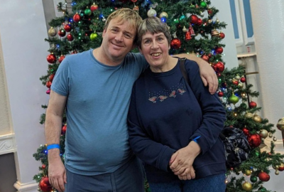 Two people standing in front of a Christmas tree smiling