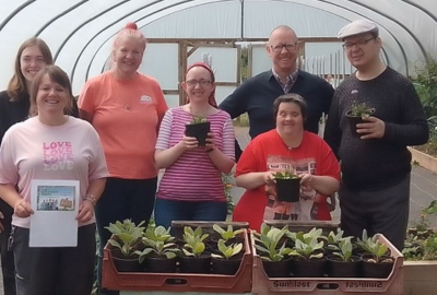 Staff and people we support standing together holding plants in a polytunnel