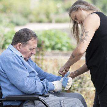 A staff member helping a person we support put gardening gloves on