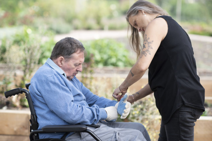 A staff member helping a person we support put gardening gloves on