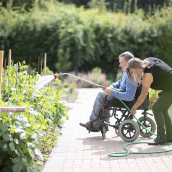 A person we support watering plants with a hose in a wheelchair