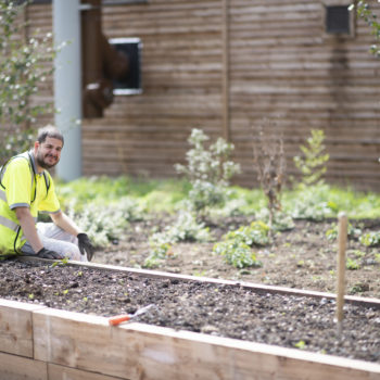 A person we support sitting by a flower bed in a garden smiling