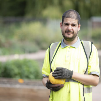 A person we support in a garden smiling at the camera holding a small orange pumpkin