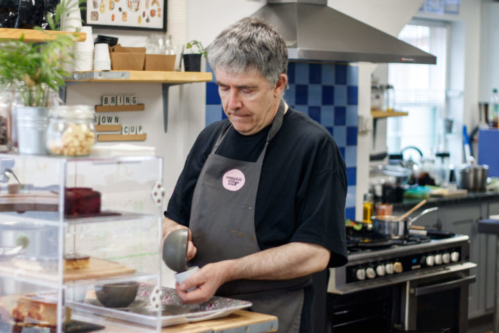 A man making a coffee in one of our cafes wearing a grey apron