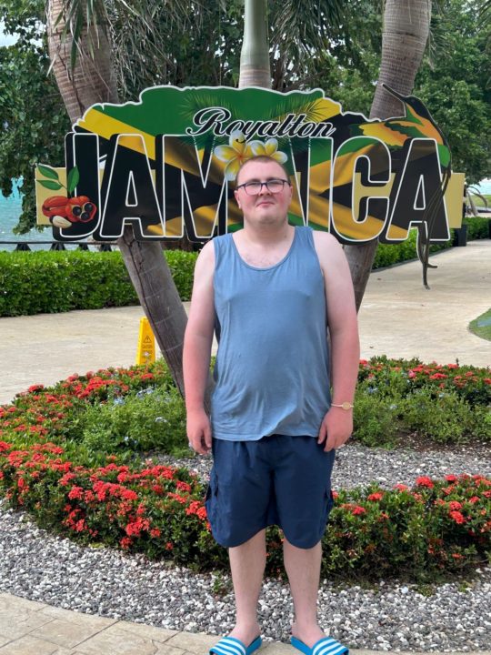 A person we support in Jamaica standing in front of a sign