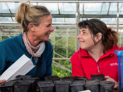 One of our support workers and a person we support enjoying planting in one of our greenhouses